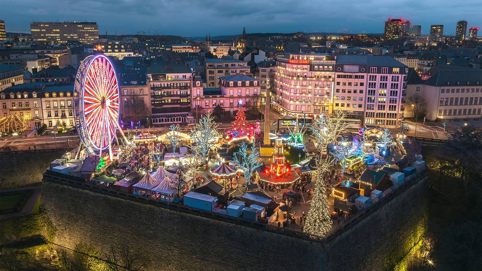 Luxembourg's Christmas market at dusk on the Place de la Constitution, the big wheel lit above the old city walls.